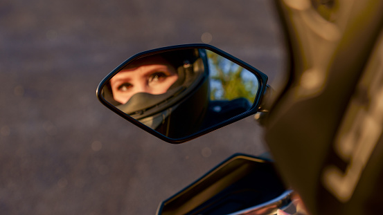 The girl on a motorcycle. Blurred reflection in mirror. Selective focus. Displaying girls in the mirror of the motorcycle. Very beatiful eyes