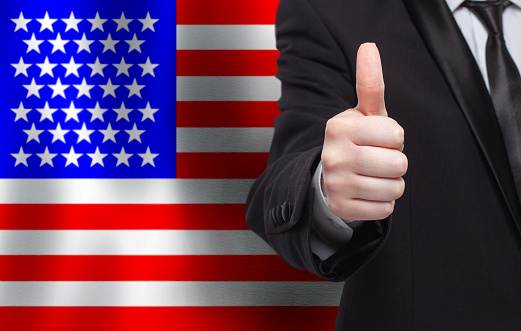 American concept. Businessman showing thumb up on the background of flag of USA