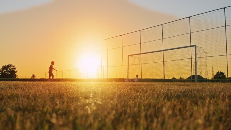 SLOW MOTION Boy taking penalty kick and missing goal on field at dusk