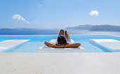 Young Asian women on vacation at Santorini relaxing in swimming pool looking out over Caldera ocean