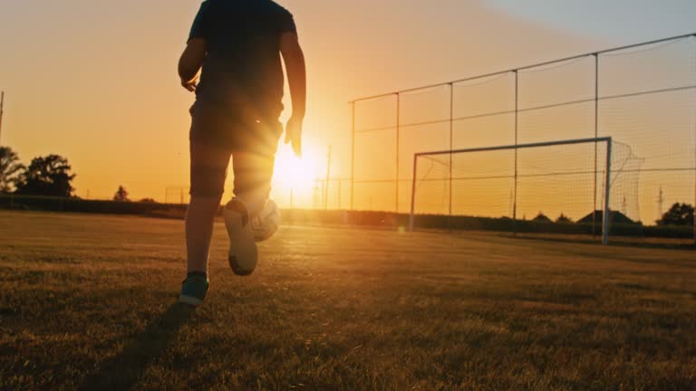 SLOW MOTION Boy playing football in field at dusk