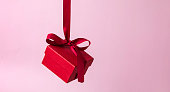Red gift box with a ribbon hangs on a pink background. Gift on Valentine's Day, Women's Day,