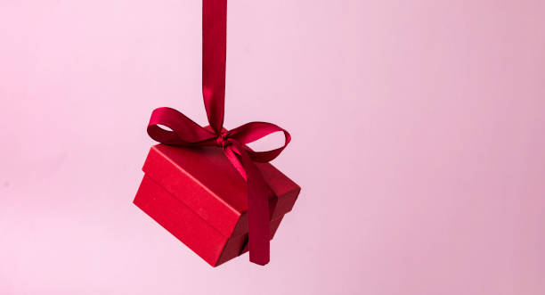 Red gift box with a ribbon hangs on a pink background. Gift on Valentine's Day, Women's Day, stock photo
