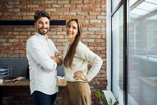 Portrait of two successful business people standing together at office. Businesswoman and businessman work colleagues posing at small office