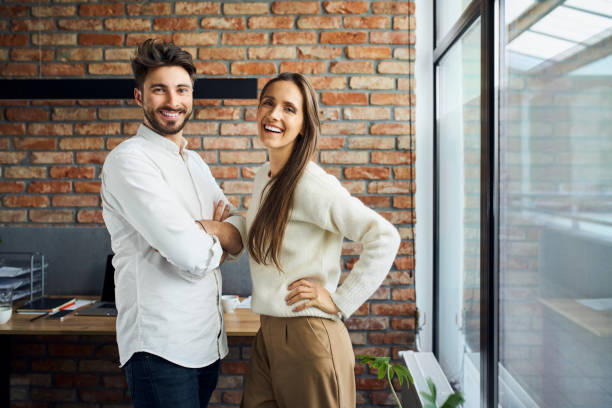 Portrait of two successful business people standing together at office. Businesswoman and businessman work colleagues posing at small office stock photo