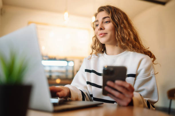 istock Woman sitting at her desk in cafe, typing text message using smart phone while working. 1460435415
