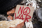 No War placard with peace sign on debris of bombed, destroyed, ruined building.