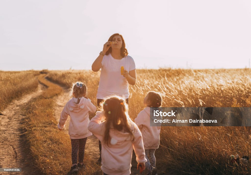 Mother and daughters triplets family time, blowing bubbles at sunset outdoors Mother Stock Photo