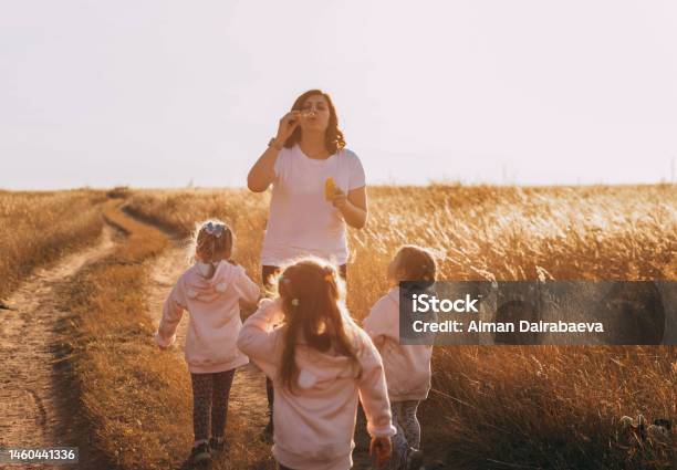 Mother And Daughters Triplets Family Time Blowing Bubbles At Sunset Outdoors Stock Photo - Download Image Now