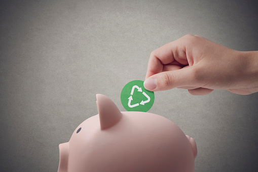 Woman putting a coin with recycling symbol in a piggy bank, green investing concept