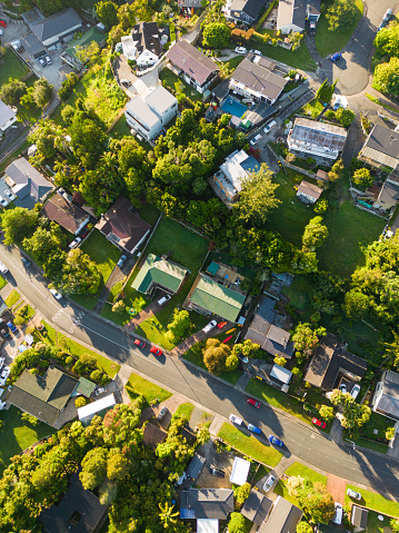 Aerial drone view of a suburban city crowded by houses and mode of transport and greenery.