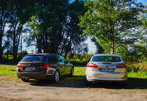Sarbinowo, Poland – August 06, 2018: The two cars parked by green trees close to on a sunny day in Sarbinowo, Poland