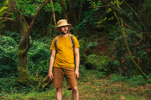 A Caucasian male wearing yellow outfit and a backpack walking in a forest exploring the wilderness