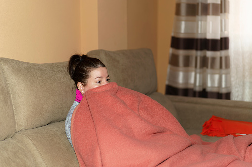 Woman sitting on the sofa wrapped in a blanket without heating