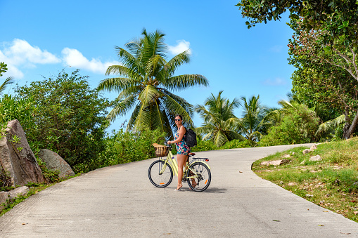 A closeup of a young woman sitting on bicycle in middle of path tropical island La Digue on Seychelles