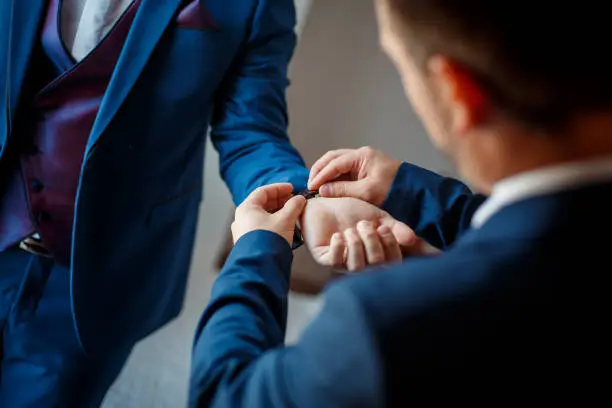 A selective focus shot of a best man putting a watch around the groom's wrist on a wedding