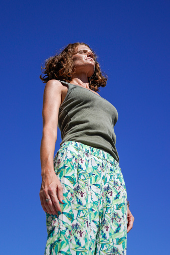 A vertical shot of a Caucasian woman meditating under a clear blue sky