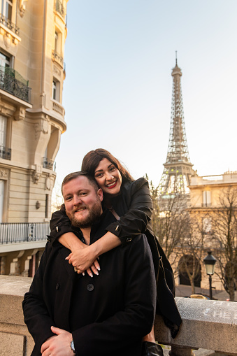 A vertical shot of the happy couple taking pictures with Eiffel Tower on the background, Paris, France