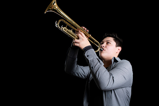 A young Caucasian teenager energetically playing trumpet on black background