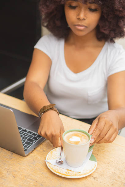 istock Young Afro woman in a coffee shop working online at her computer and drinking coffee. 1460459018