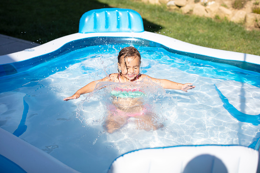 Little girl enjoying the hot summer in her blue and white inflatable swimming pool escaping the heat in Germany