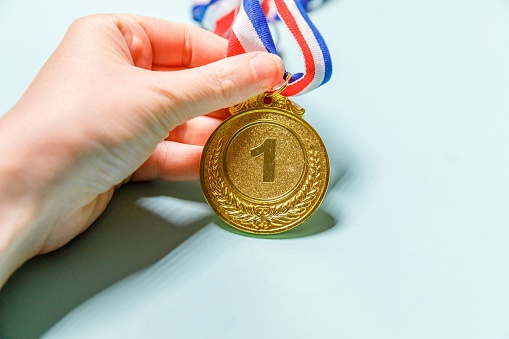 A gold medal engraved with 2024.  A red, white, and blue ribbon is attached to the medal that rests on a background that graduates from gray to black.