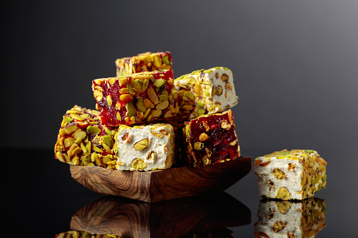 Traditional Turkish delight in a wooden dish on a black reflective background.