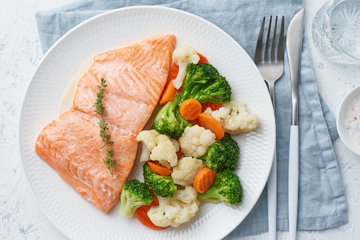 A closeup of steamed salmon and vegetables on a white plate