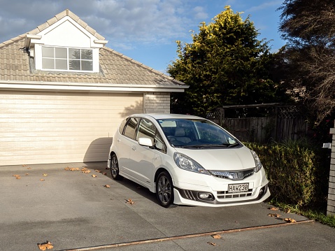 Auckland, New Zealand – May 23, 2022: White Honda Jazz car in front of suburban garage. Auckland, New Zealand - May 20, 2022