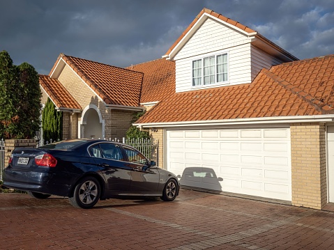 Auckland, New Zealand – May 23, 2022: BMW 323i car in front of white suburban house with garage. Auckland, New Zealand - May 20, 2022