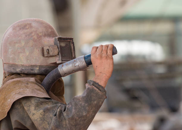A tired senior construction site worker standing outdoors with a helmet in his hands and wiping the sweat from his forehead. A tired worker at the construction site.