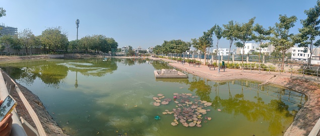 A panoramic view of a lake in a park surrounded by green nature on a bright, sunny day