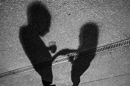 Shadows of a couple shaking hands and holding cups on an asphalt groun