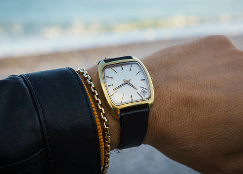 Vintage wrist watch and gold bracelet on man's arm, close up