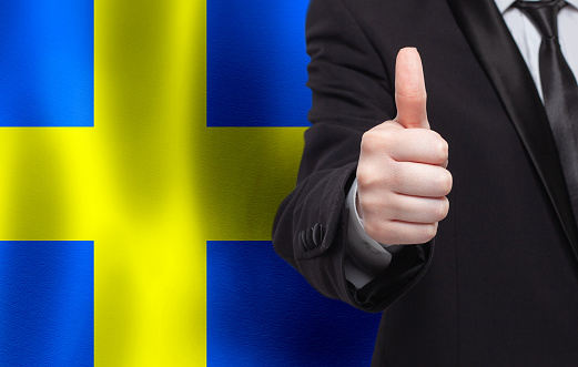 Swedish concept. Businessman showing thumb up on the background of flag of Sweden