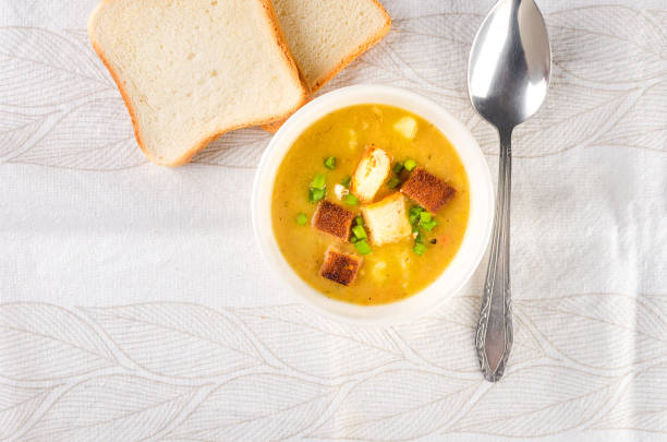 Split pea soup with croutons and green onion in a bowl on white table. Healthy homemade thick soup in white bowl for winter lunch.
