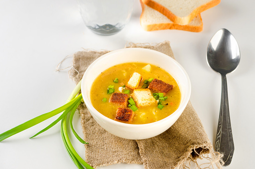 Split pea soup with croutons and green onion in a bowl on white table. Healthy homemade thick soup in white bowl for winter lunch.