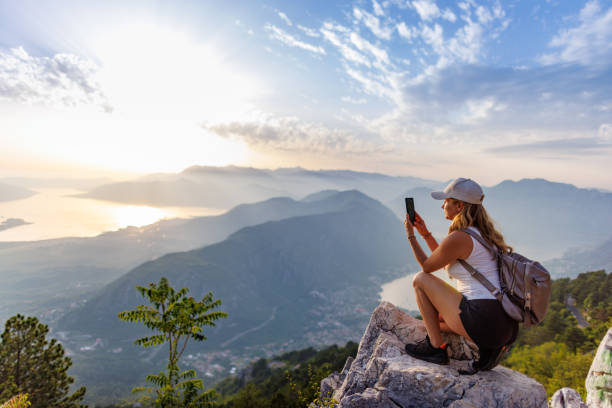 A happy girl with a backpack photographs the seascapes of Montenegro from the top of the mountain stock photo