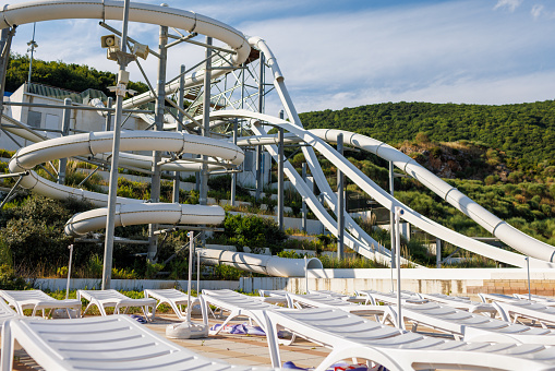 Empty indoor mountain summer water park with high extreme winding white slides and white folded sun loungers in spaced rows