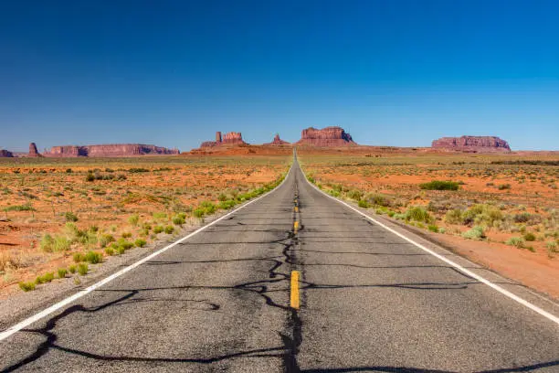 Clear blue sky over a road in rough desert landscape with rock formations at Monument Valley in Arizona.