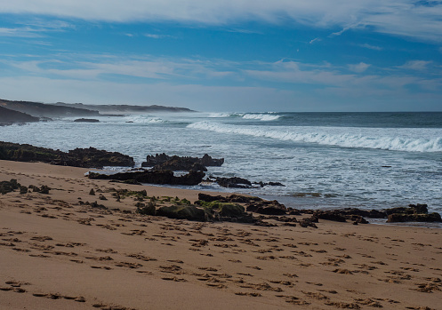 View of empty Praia da Ilha do Pessegueiro sand beach with ocean waves and sharp rock and cllifs at wild Rota Vicentina coast near Porto Covo, Portugal.