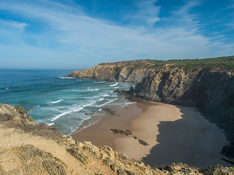 Vista de la playa vacía de Praia das Bernosas con olas del océano, acantilados y piedras, arena dorada húmeda y vegetación verde en la costa salvaje de Rota Vicentina, Odemira, Portugal. photo