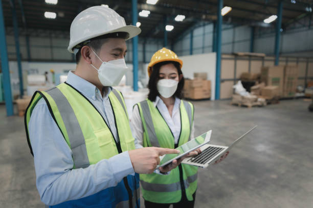 istock Factory manager and engineer in  medical mask and safety protective suite using computer laptop and digital tablet working discuss together 1460490625