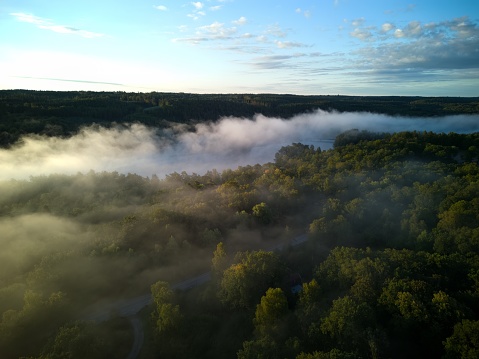 Aerial drone image of a beautiful foggy sunrise over a lake and forest in Sweden. Image captured nearby Simlangsdalen, Halmstad, Halland. Beautiful cloudscape, forest and fog in the valleys. Over the clouds. Colourful background image. Vast open landscape.