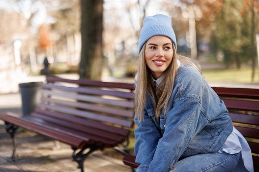 Beautiful young woman sitting and relaxing on bench in city park