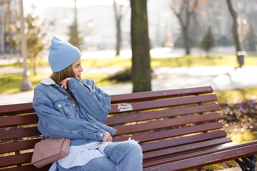 Beautiful young woman sitting and relaxing on bench in city park