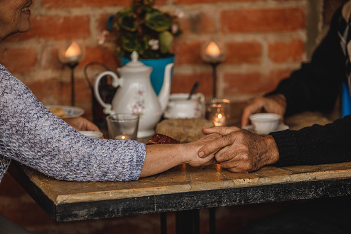 Cut out shot of affectionate. unrecognizable senior married couple  holding hands and bonding while enjoying afternoon tea in a romatic setting on their patio.