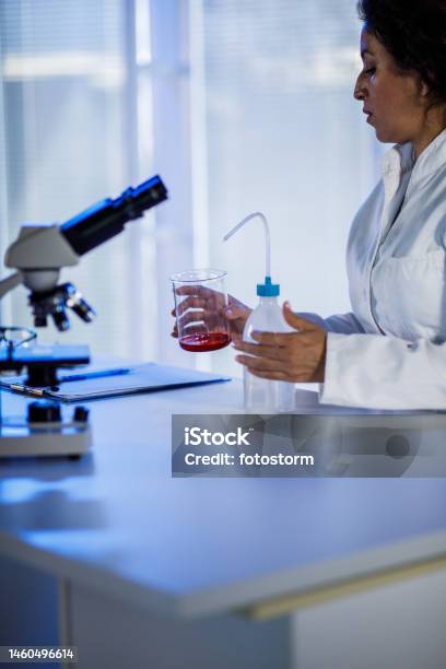 Female Scientist Adding Liquid Into A Beaker With Wash Bottle She Is Using Stock Photo - Download Image Now