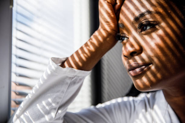 istock Female scientist standing by the window, blind shades playing on her face while she takes a break from work 1460498531