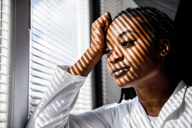 istock Female scientist standing by the window, blind shades playing on her face while she takes a break from work 1460498533